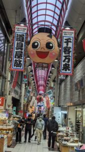 Marché couvert Grosse tête de personnage en devanture d'un marché à Dotonbori, Osaka, avec la rue animée en arrière-plan