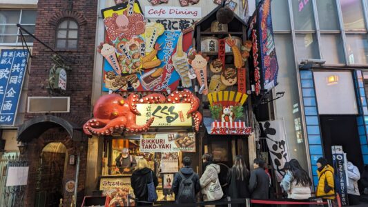Takoyaki & Line Up Façade d'un restaurant de takoyaki à Dotonbori, avec une enseigne colorée et des décorations typiques