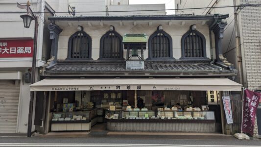 Maison traditionnelle dans un quartier commerçant animé, entourée de boutiques et de restaurants