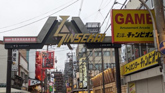 Affiche colorée et porte d'entrée emblématique de Shinsekai à Osaka, accueillant les visiteurs dans ce quartier animé