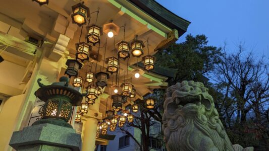 Lanternes traditionnelles et statue de lion à Osaka, photographiées en contrebas, créant une atmosphère zen et spirituelle