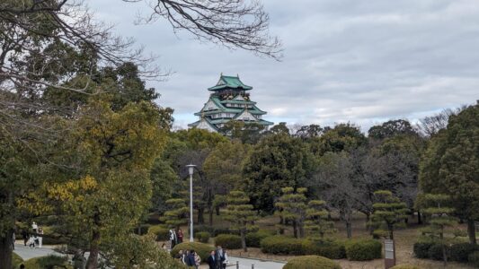 Vue du Château d'Osaka entouré de jardins verdoyants et d'arbres en fleurs, avec des visiteurs profitant du parc