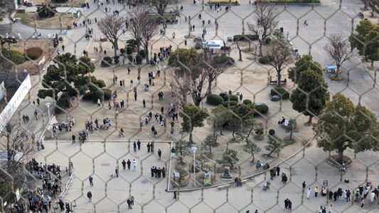 Vue de la ville d’Osaka à travers un grillage depuis le château d'Osaka, avec des gratte-ciels à l'horizon et des jardins verdoyants au premier plan