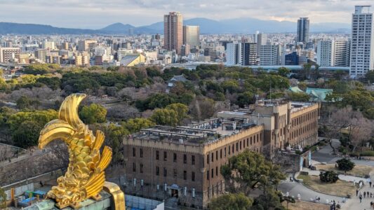 Vue panoramique du château d'Osaka avec une statuette dorée en forme de queue de poisson au premier plan