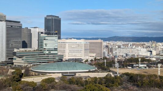 Vue panoramique du château d'Osaka avec des monuments environnants, incluant un stade au loin