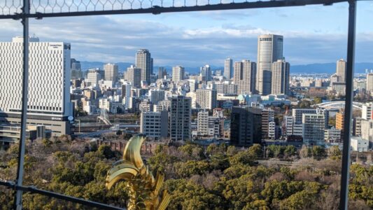 Vue panoramique du château d'Osaka avec une statuette dorée en forme de queue de poisson au premier plan