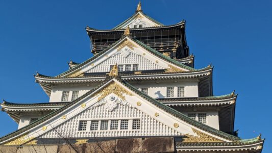 Image du château d'Osaka sous un ciel bleu éclatant, mettant en valeur son architecture majestueuse
