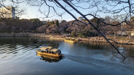 Image du château d'Osaka reflété dans l'eau d'un lac, avec un petit bateau jaune flottant à la surface
