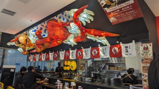 Devanture de restaurant de takoyaki Image d’un magasin à Osaka avec un énorme takoyaki et une sculpture de poulpe en façade, attirant l’attention des passants