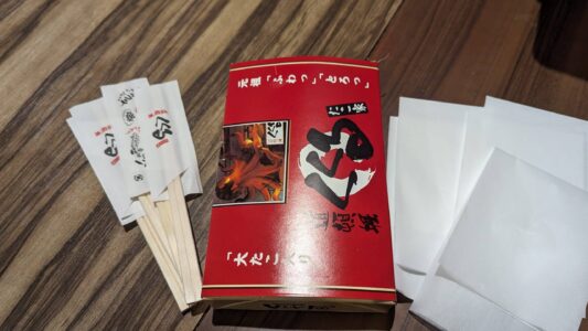 Emballage des takoyakis Image d'une boîte rouge de takoyaki à emporter, avec des baguettes posées sur le côté, lors d’un food tour à Osaka
