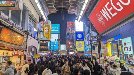 Rue bondée samedi soir dans le quartier de Dotonbori Image d'une foule animée dans la rue centrale de Dotonbori à Osaka, avec des enseignes lumineuses et des restaurants en arrière-plan