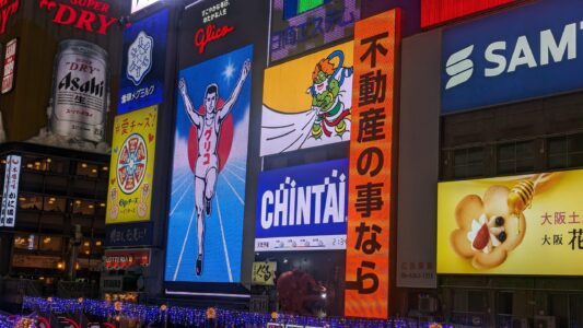 Image des célèbres enseignes Glico illuminées dans le quartier de Dotonbori à Osaka, créant une ambiance festive la nuit
