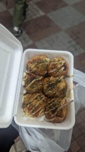 Image de takoyaki servis dans un sachet pratique à emporter, garnis de sauce, mayonnaise et flocons de bonite, parfaits pour une dégustation en pleine rue d'Osaka