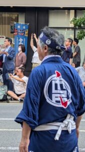 Texte alternatif : Un homme en costume traditionnel japonais est vu de dos, regardant un char illuminé et coloré lors du Nebuta Matsuri à Aomori, créant une scène immersive et festive dans le défilé nocturne.