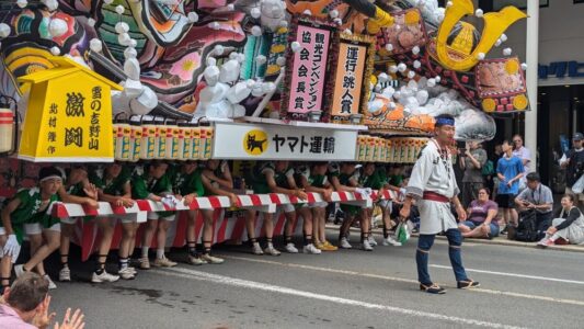Char Nebuta en plein jour. Premier plan : homme avec un sifflet menant le groupe