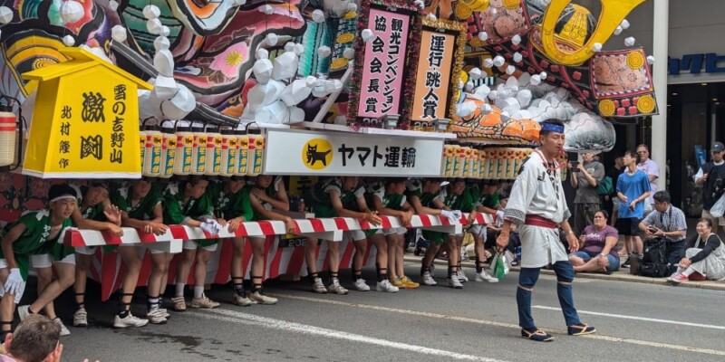 Char Nebuta en plein jour. Premier plan : homme avec un sifflet menant le groupe