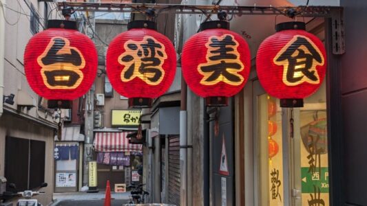 Rangées de lanternes japonaises traditionnelles en papier, suspendues et illuminées, créant une atmosphère paisible. Les caractères japonais et les motifs décoratifs reflètent la culture et l'art du Japon