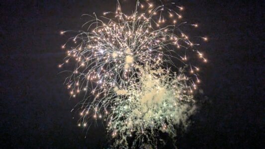 "Défilé nocturne des chars Nebuta illuminés avec des feux d’artifice violets et verts éclatant en arrière-plan lors du festival Nebuta d’Aomori