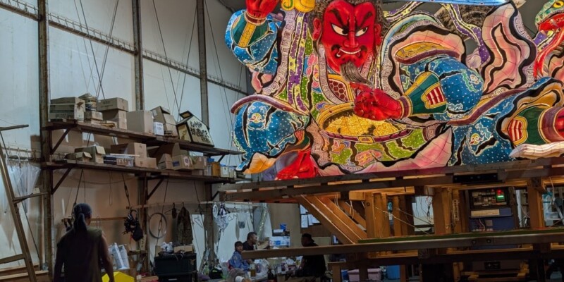 Photographie pendant 2 jours "Photographie de chars Nebuta à l'arrêt pendant le festival, ornés de décorations colorées et illuminés, avec des participants en costumes traditionnels autour