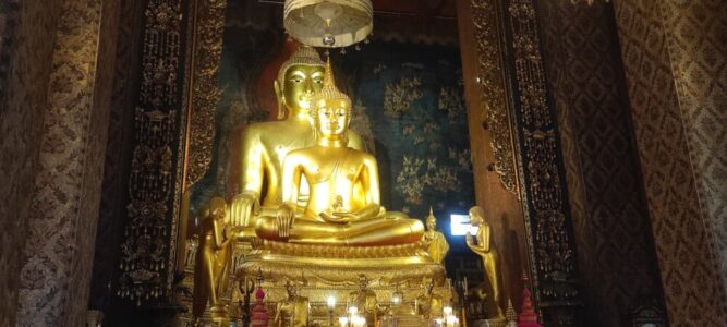Intérieur d'un temple à Bangkok, avec plusieurs statues de Bouddha dorées entourées de motifs ornés et de décorations colorées