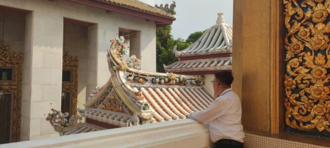 Un homme thaïlandais en chemise blanche observe les temples environnants, entouré de l'architecture richement décorée et de la sérénité du site