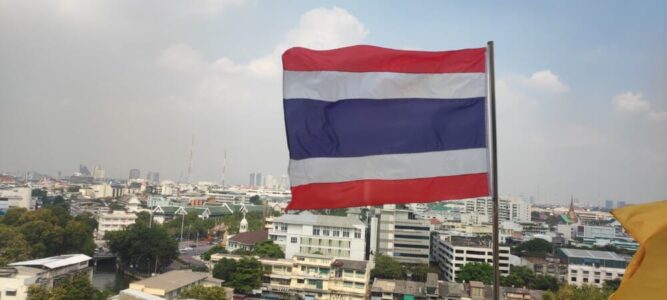 Vue panoramique de Bangkok, avec le drapeau thaïlandais flottant au premier plan, surplombant la ville et ses gratte-ciels