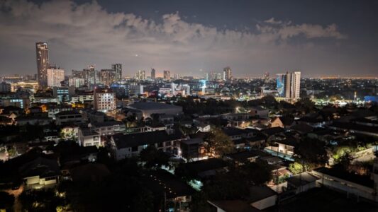 Une vue panoramique de Bangkok illuminée la nuit, mettant en avant l'architecture alternative avec des bâtiments modernes aux formes audacieuses et aux lumières colorées, contrastant avec les structures traditionnelles thaïlandaises