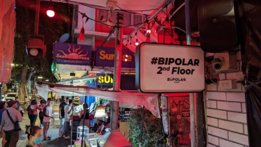 Vue nocturne d'un panneau lumineux du bar "Bipolar" dans le quartier rouge de Bangkok, avec des néons colorés et une ambiance animée
