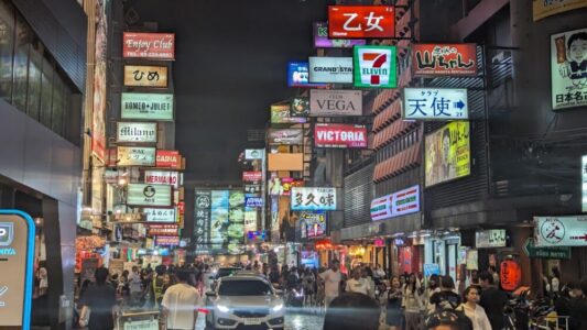 Rue de Bangkok la nuit dans un quartier rouge, illuminée par de nombreuses enseignes