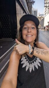 Inès portant une casquette, affichant un sourire et montrant son tatouage