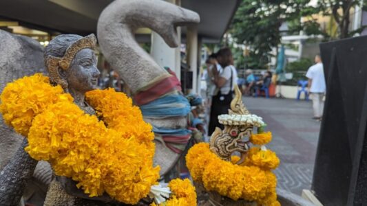 Gros plan d'une statue d'éléphant au temple, ornée de fleurs et d'une couronne jaune, avec une scène de vie animée en arrière-plan