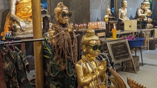 Deux statues de Bouddha dorées portant des lunettes de soleil, priant comme des stars, dans un temple de Bangkok