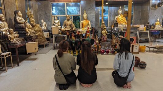 Trois femmes en prière dans un temple moderne, avec des statues en arrière-plan