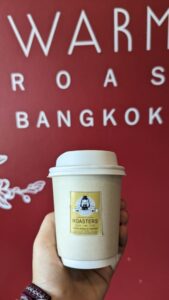 Tasse de café tenue dans la main, avec un fond rouge dans un café à Bangkok