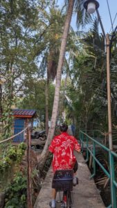 Personne en chemise rouge sur un pont avec des fleurs, faisant du vélo dans le parc Bangkachao à Bangkok, avec de la végétation en arrière-plan