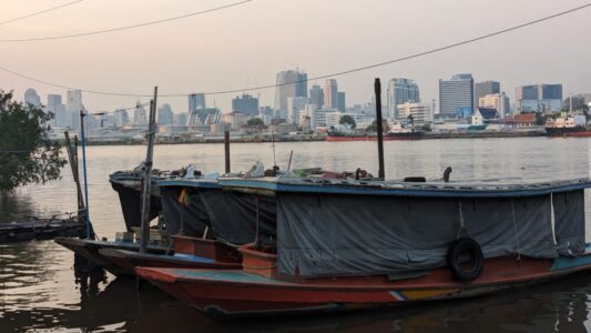 Bateau sur l'eau au coucher du soleil, avec la rive opposée de Bangkachao en arrière-plan