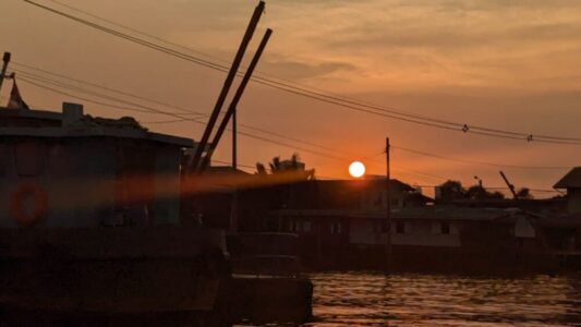 Bateau au coucher du soleil sur le fleuve Chao Phraya, avec des bâtiments traditionnels en arrière-plan