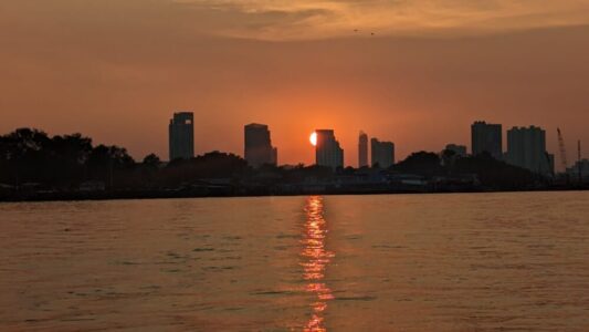 Bateau au coucher du soleil sur le fleuve Chao Phraya, avec des gratte-ciels en arrière-plan
