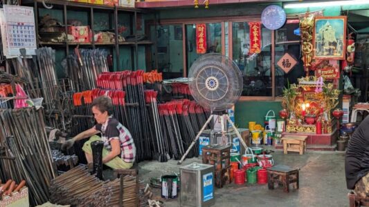 Femme assise à l'intérieur d'un magasin de ferraille à Chinatown, Bangkok, entourée d'objets métalliques