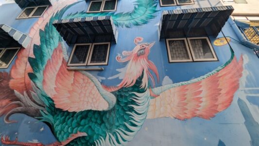 Illustration de street art représentant un oiseau déployant ses ailes, dans des teintes de rose et de bleu