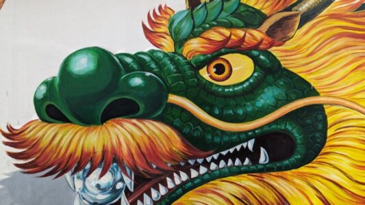 Gros plan sur une œuvre de street art représentant un dragon vert et jaune avec une moustache, sur un mur à Bangkok
