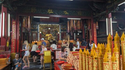 Illustration de l'intérieur d'un temple chinois à Bangkok avec des bougies allumées au premier plan et des statues et ornements en arrière-plan