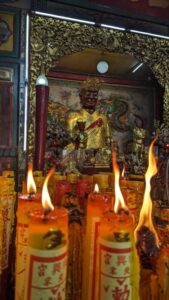Illustration d'un temple à Bangkok avec des bougies allumées au premier plan et une statue chinoise en arrière-plan