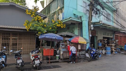 Illustration de plusieurs marchands de street food à Bangkok, sous des parasols colorés, entourés de câbles électriques