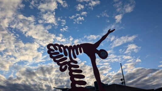 Un street art vibrant représentant un homme dansant entouré d'une forme en ressort, avec un ciel bleu éclatant en arrière-plan. L'œuvre capture le mouvement et l'énergie créative