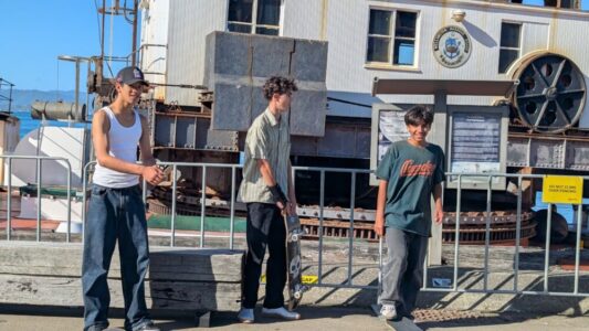 Trois jeunes hommes pratiquent du skateboard dans une rue animée de Wellington
