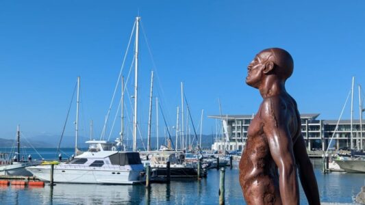 Statuette en bronze au port de Wellington sous un ciel bleu. Bateaux amarrés en arrière-plan