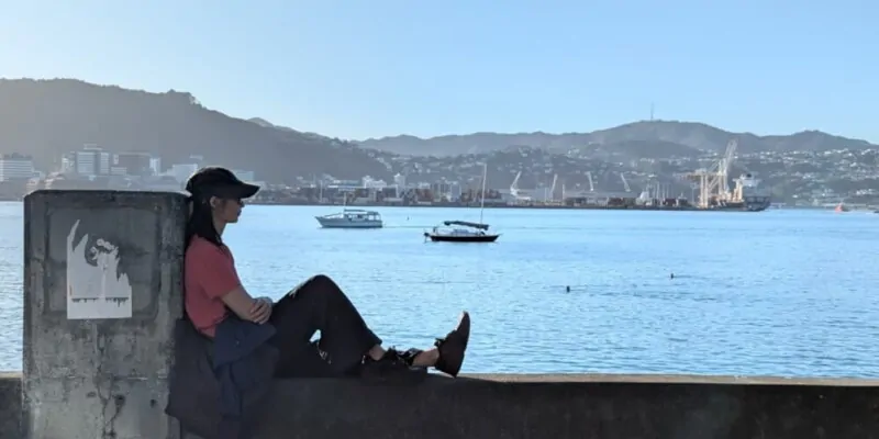 Femme détendue en casquette au port d’Oriental Bay, Wellington. Vue panoramique sur la plage en arrière-plan