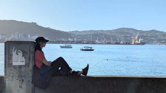 Femme détendue en casquette au port d’Oriental Bay, Wellington. Vue panoramique sur la plage en arrière-plan