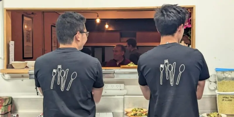Deux volontaires de dos à Wellington, en tee-shirts noirs avec des couverts imprimés. Ils assurent le service lors d’un événement